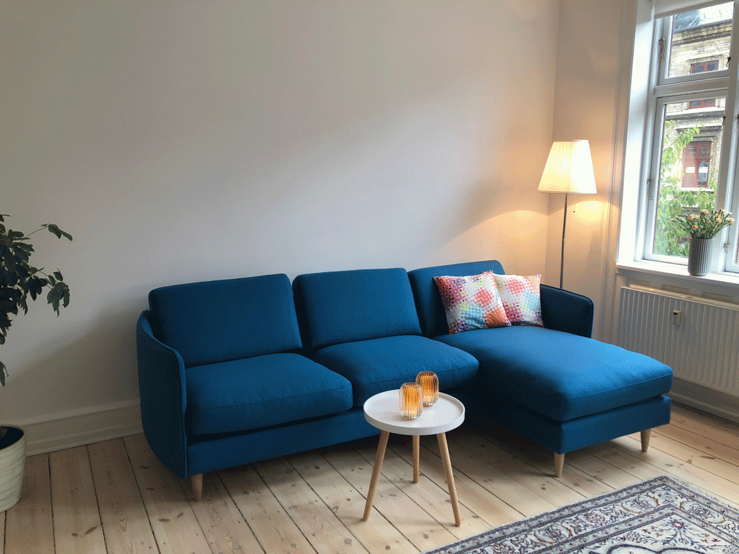 Stueindretning med feng shui. Blå Chaiselong sofa med rundt hvidt trebenet sofabord og farverige puder.