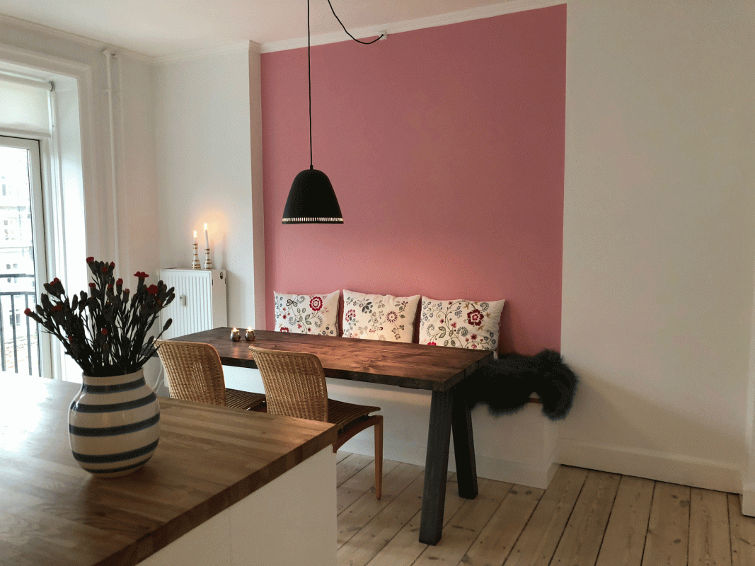 Stueindretning med feng shui. trætema med træborde, træstole, køkkenbord af træ og lyserød væg med farverige puder og sort lampe