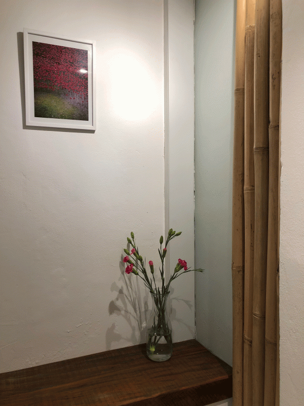 vase på træhylde med lyserøde blomster og bambuspinde, samt billede med lyserøde træer på hvid væg